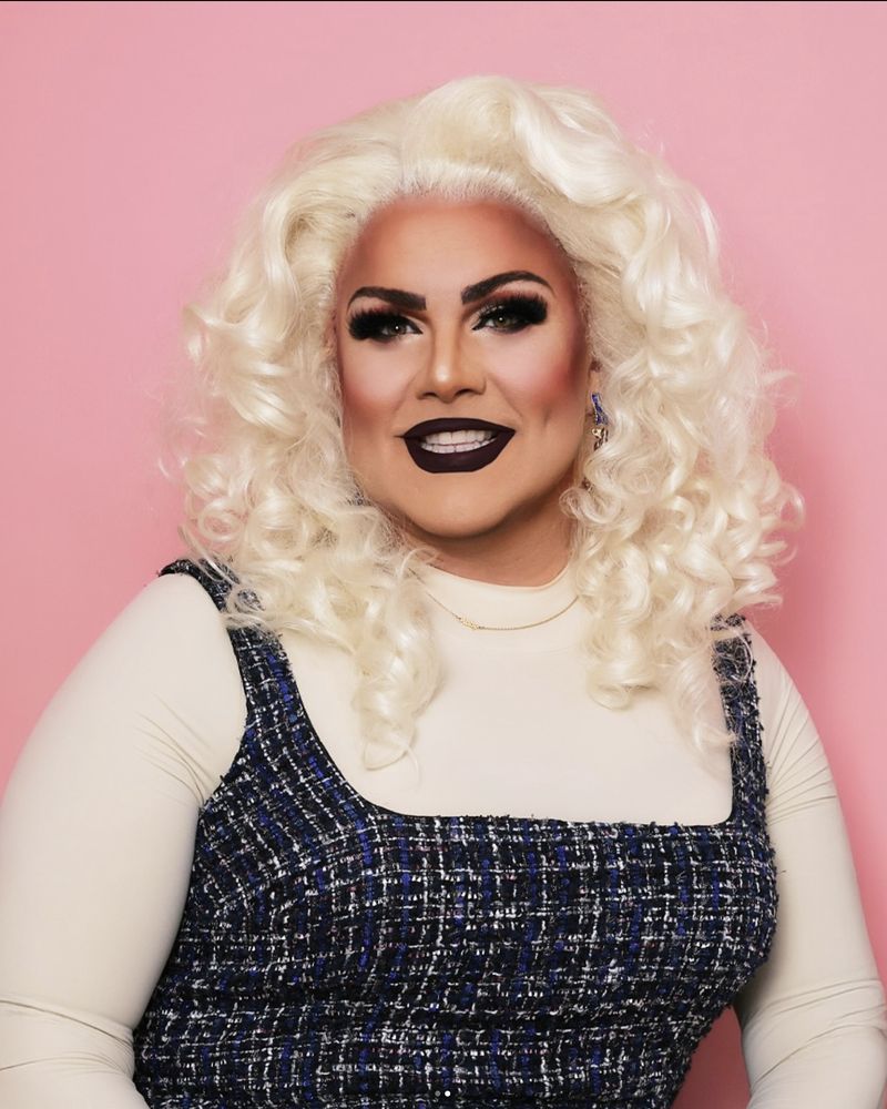 Abby Cummings smiling in a tweed dress with platinum curls against a soft pink backdrop