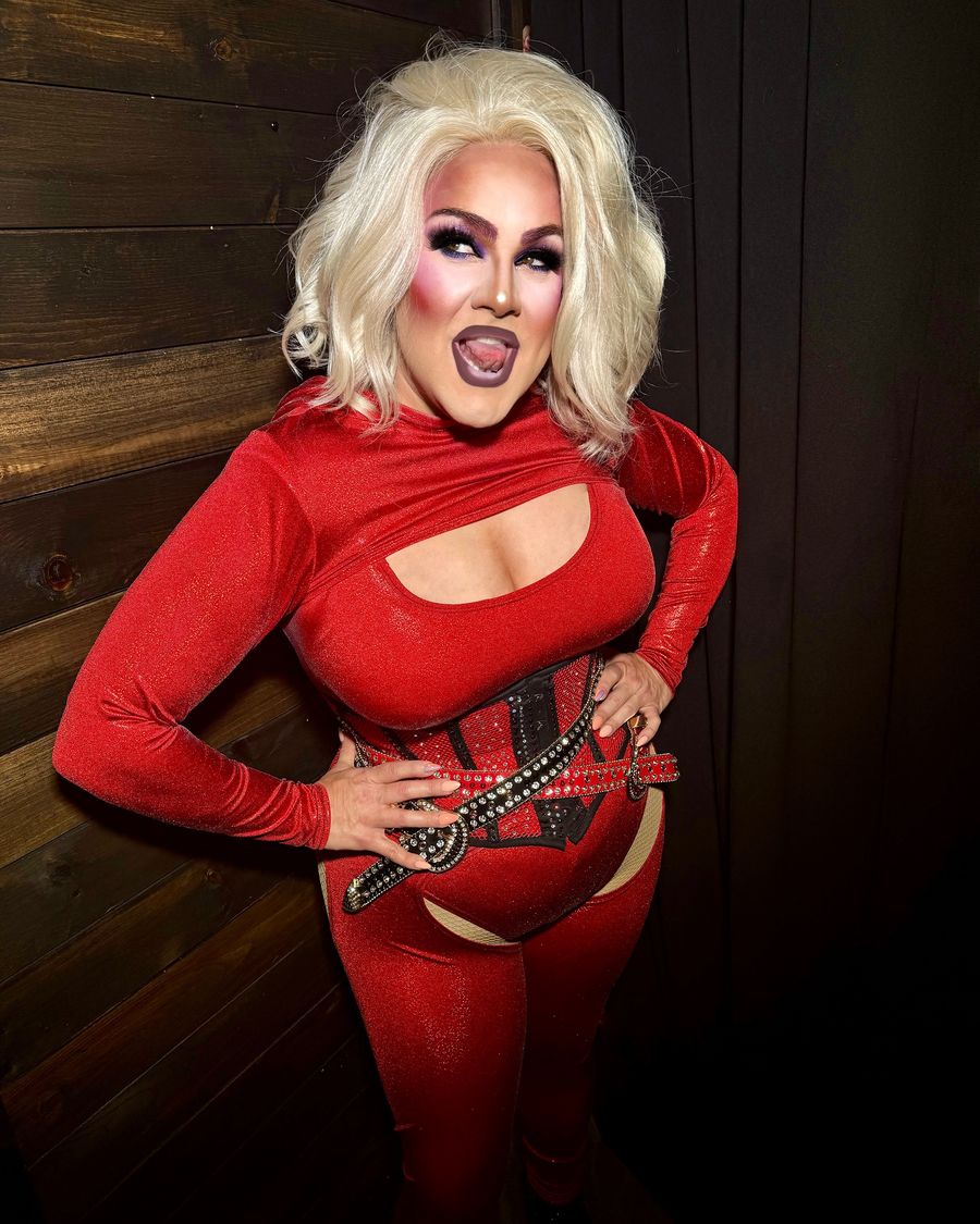 Abby Cummings in red velvet with a studded corset, grinning, hand on hip