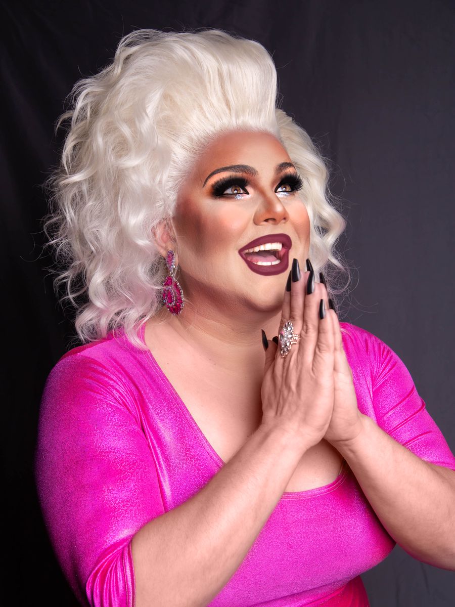Abby Cummings, a Boston drag entertainer with platinum hair and a pink dress, laughing with her hands pressed together
