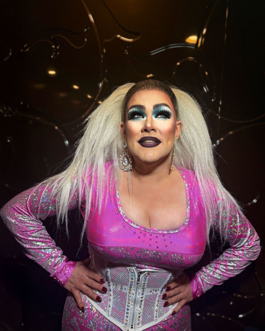 Abby Cummings in a pink corseted costume, hands on hips, under warm stage lights