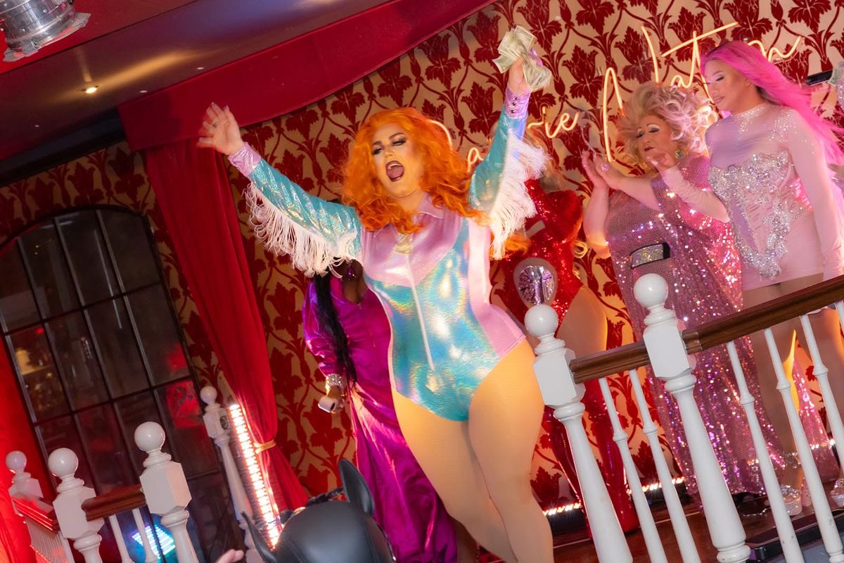 A drag brunch finale on stage in Boston, performers mid-number under red and pink lights